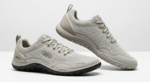 A pair of light grey Xero Shoes featuring mesh uppers, lace closures, and textured rubber soles. Engineered for walking, they provide all-day comfort with ventilation holes and a minimalistic style. The "Xero" brand name is displayed on the shoes.