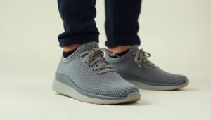 A person wearing dark pants and light grey Nexus Knit minimalist footwear by Xero Shoes with white soles, standing on a light surface. The shoes have laces and a textured pattern, emphasising their design.